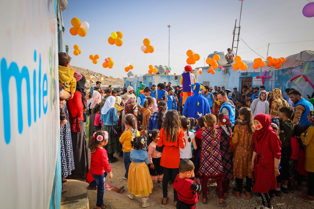 Lively event at Syrian refugee camp with children, balloons, and volunteers creating joyful moments